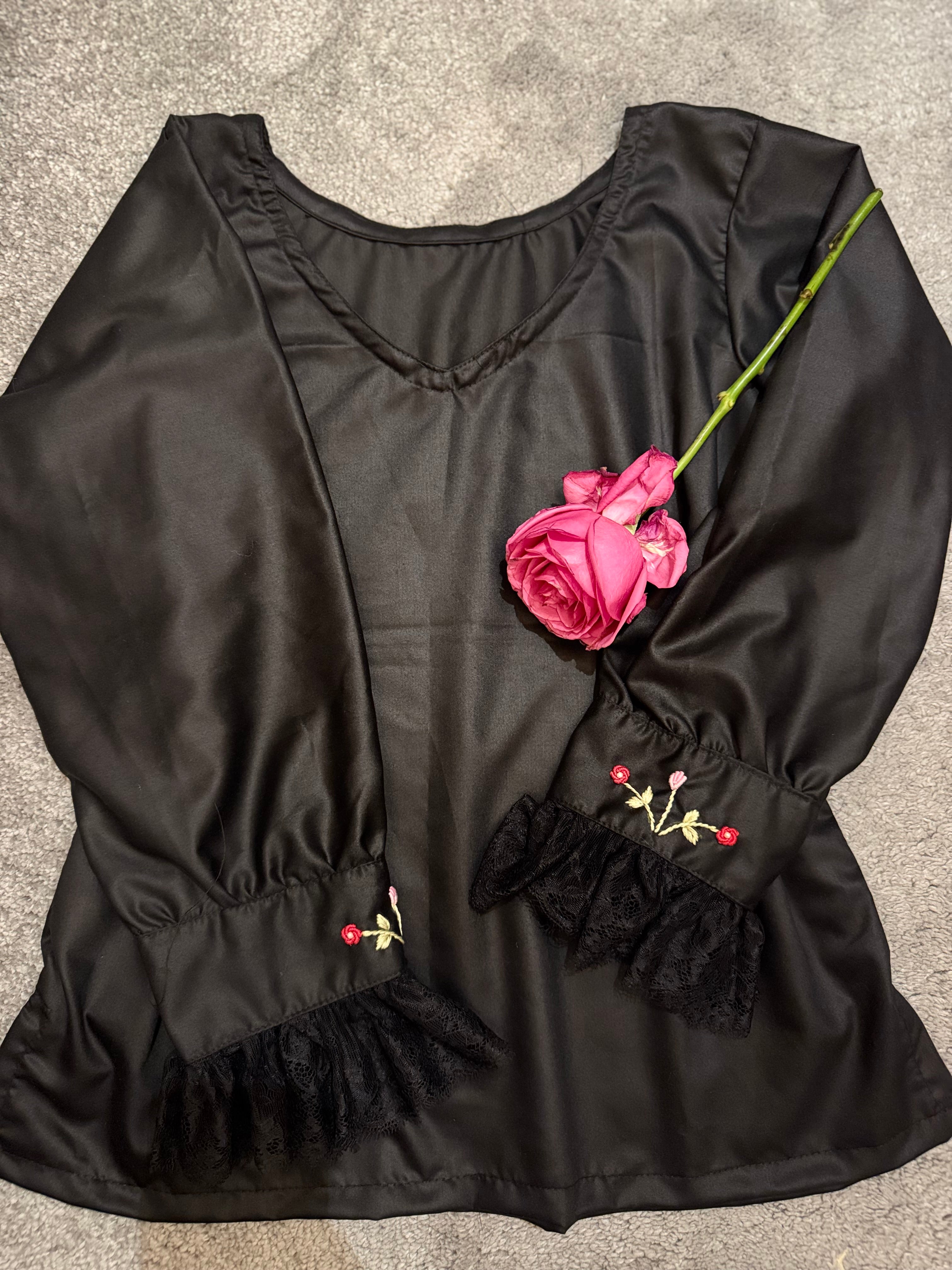 Black blouse with floral embroidery on a gray surface