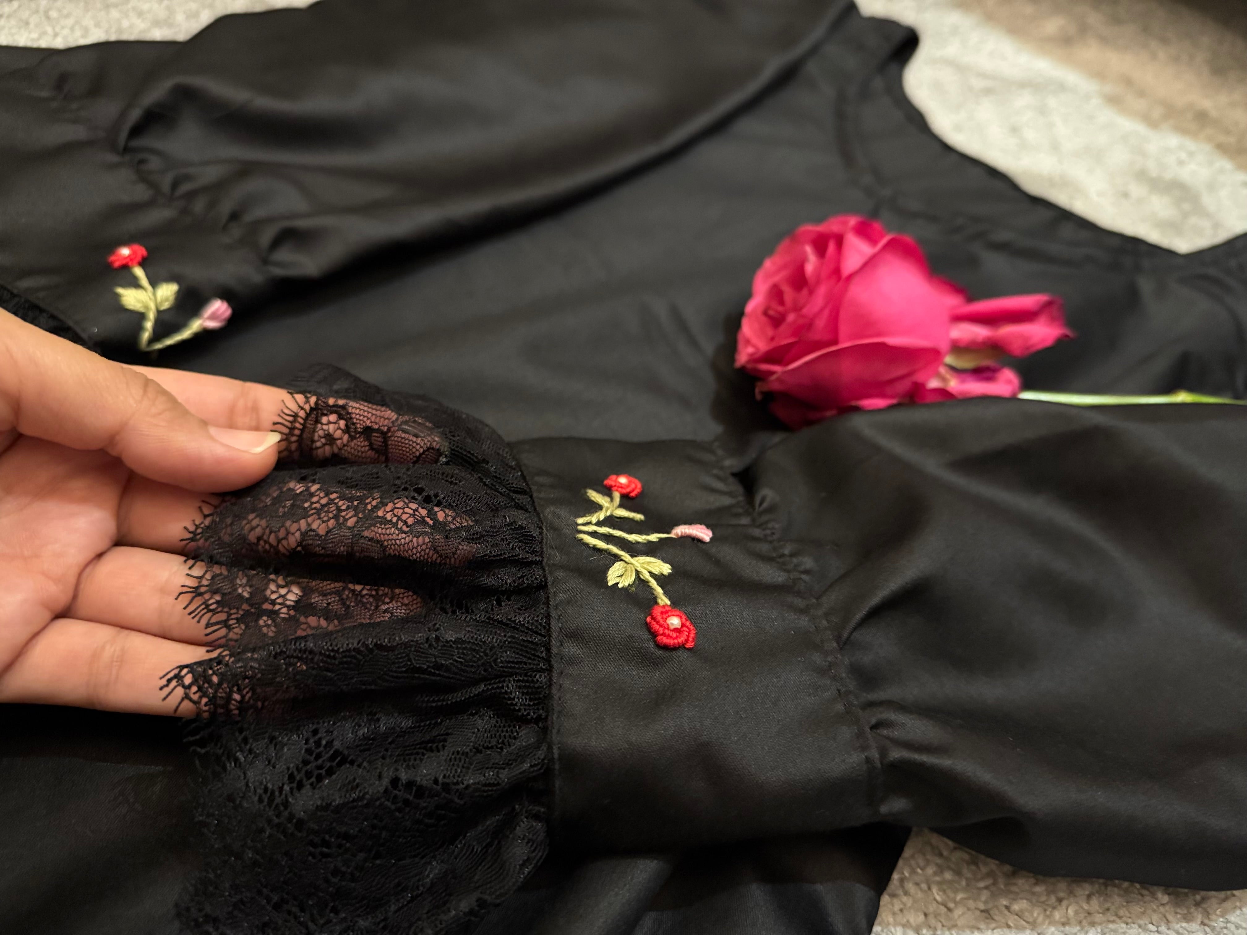 Black garment with floral embroidery held by a hand
